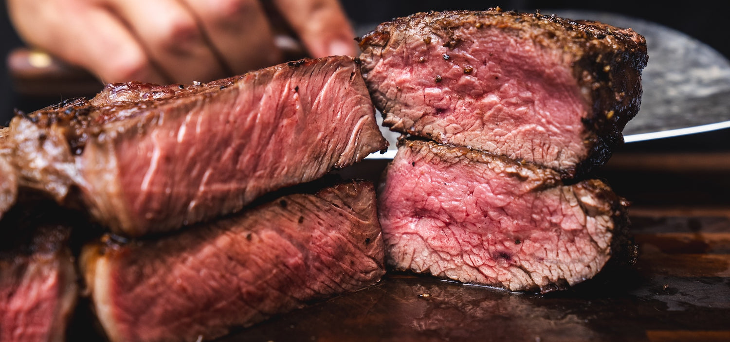 Close-up of sliced steak on a cutting board with a hand holding a knife.